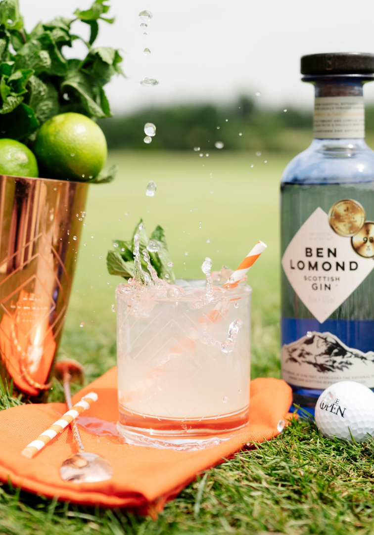 Cocktail with lime and ice, Ben Lomond Scottish Gin bottle, and golf ball on grass