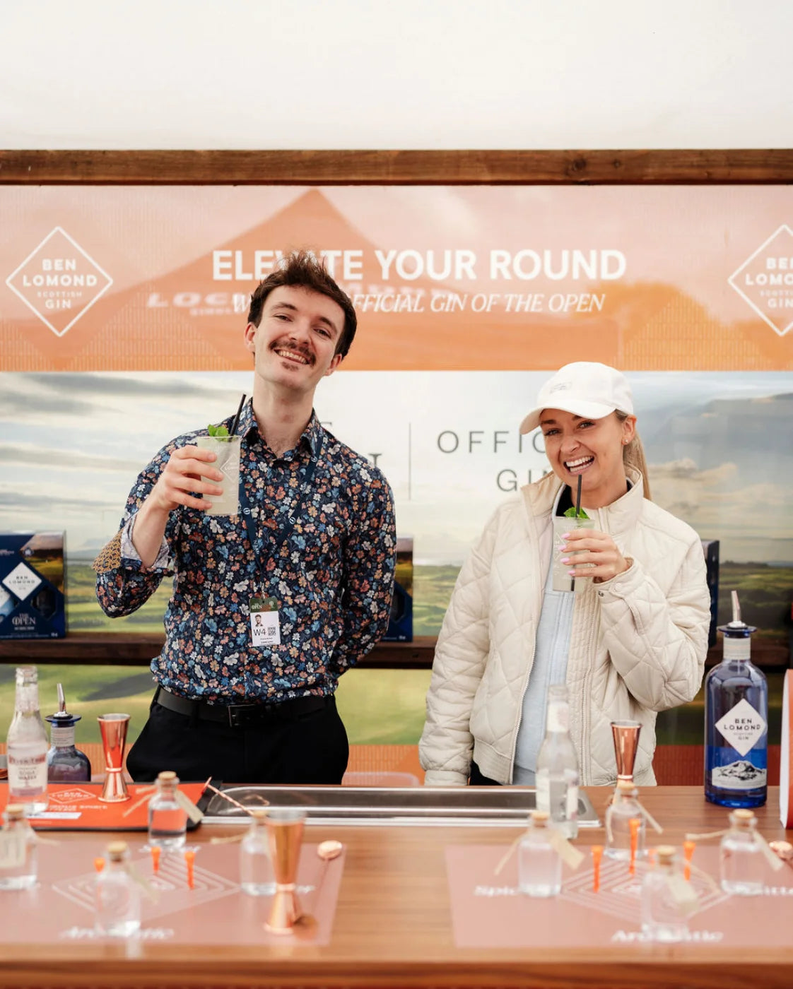Two people enjoying drinks at a bar with a promotional backdrop for Ben Lomond Gin.