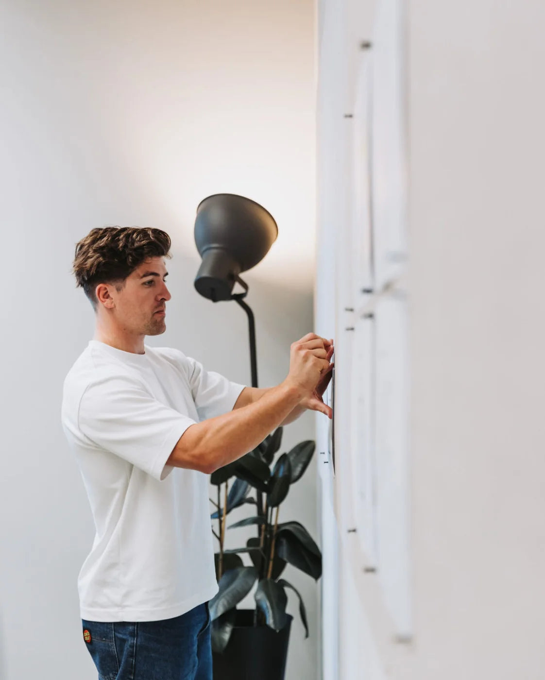 Man adjusting a light fixture in a room with a plant and lamp.
