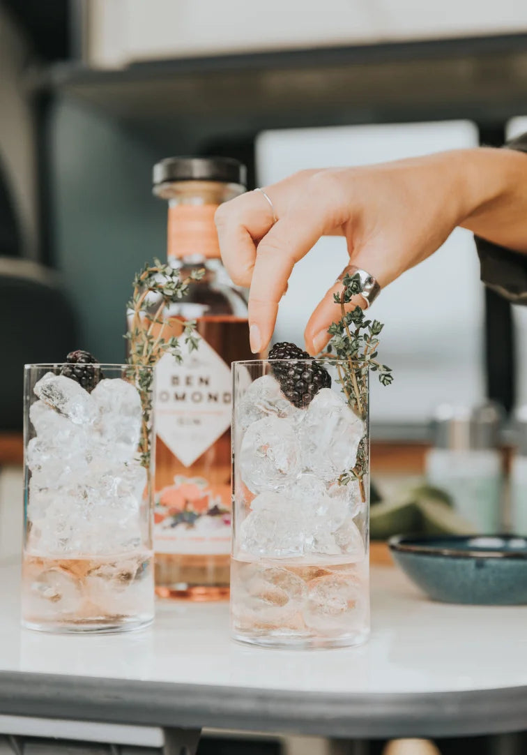 Person preparing a cocktail with ice and herbs, bottle of Ben Lomond Gin in the background.