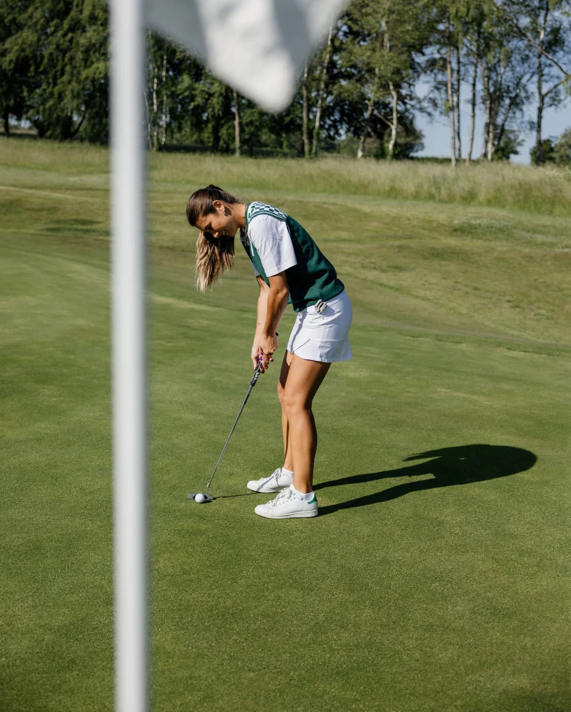 Woman playing golf on a green course with trees in the background