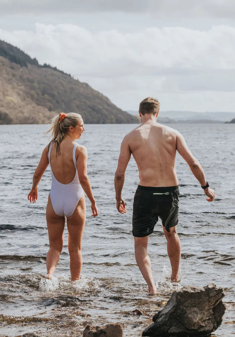 Two people walking into a lake with mountains in the background