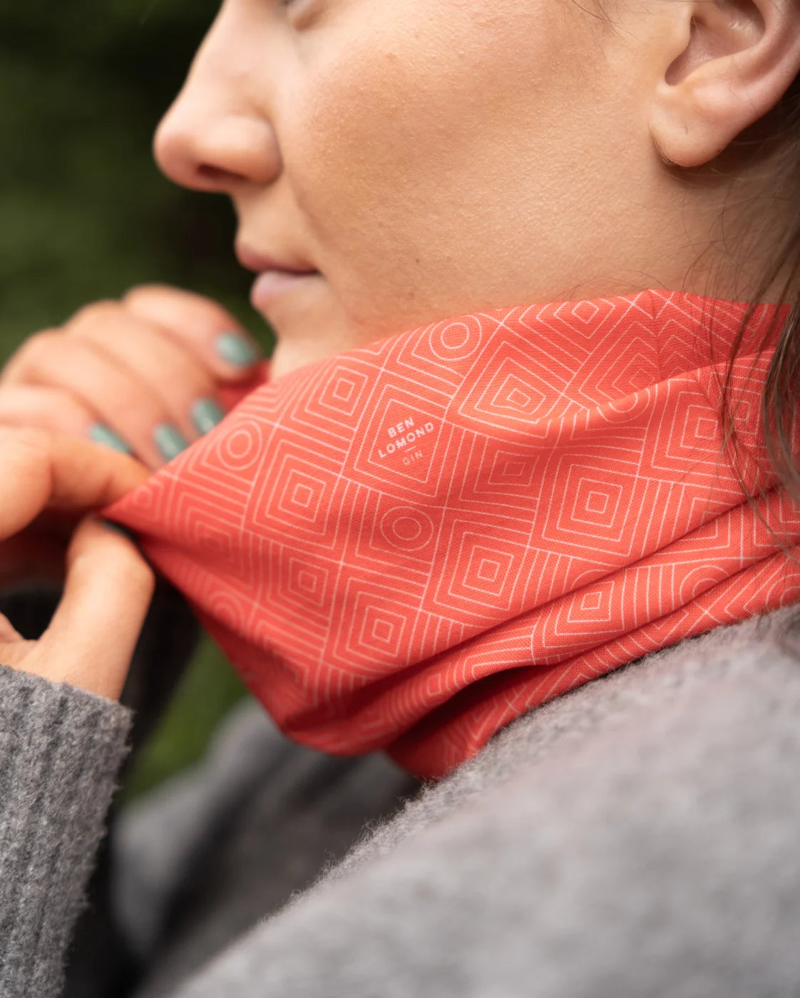 Person wearing a red patterned neck gaiter with a blurred natural background
