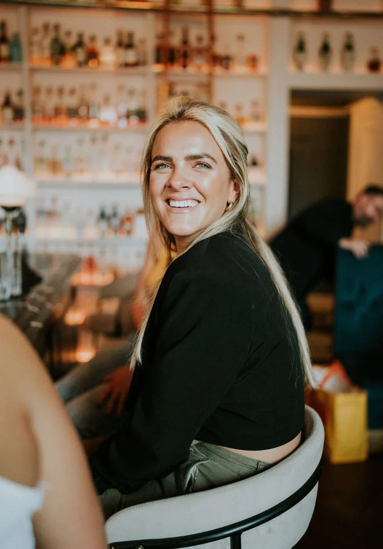 Woman sitting at a bar smiling with a well-stocked bar in the background