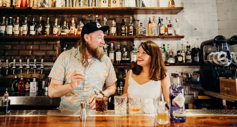 Two people at a bar with drinks in a casual setting