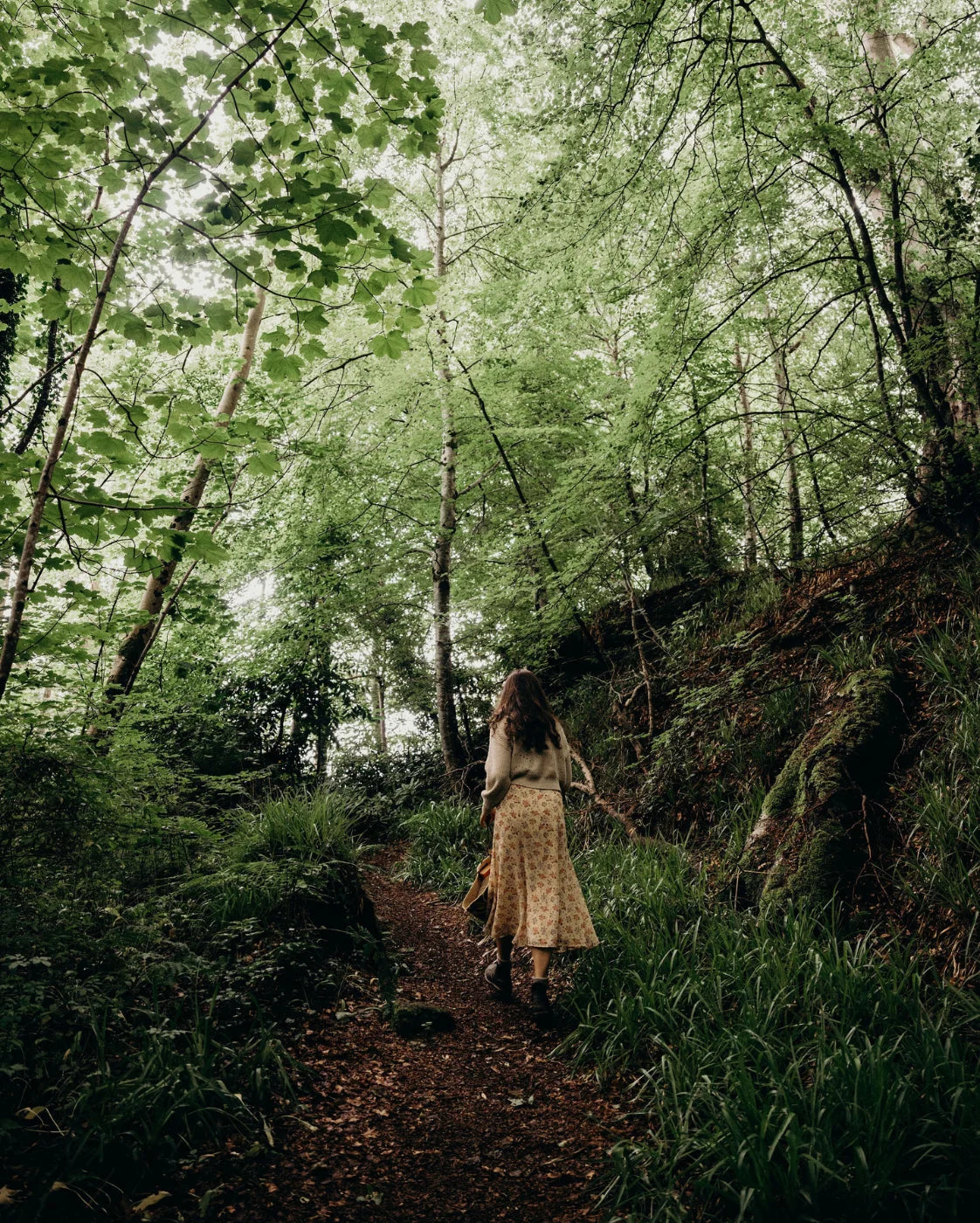 Woman walking through a forest path with greenery and trees.