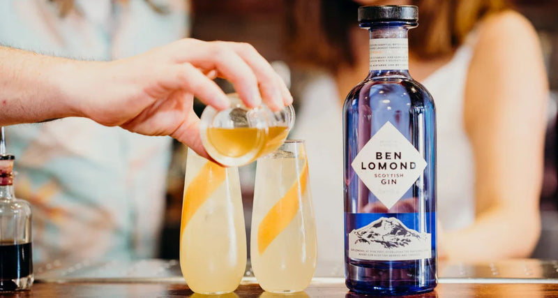 Person pouring a drink into a glass with a bottle of Ben Lomond Gin on a table.