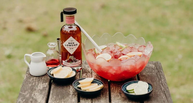 Bottle of Ben Leonard Gin with a punch bowl and ingredients on a wooden table outdoors.