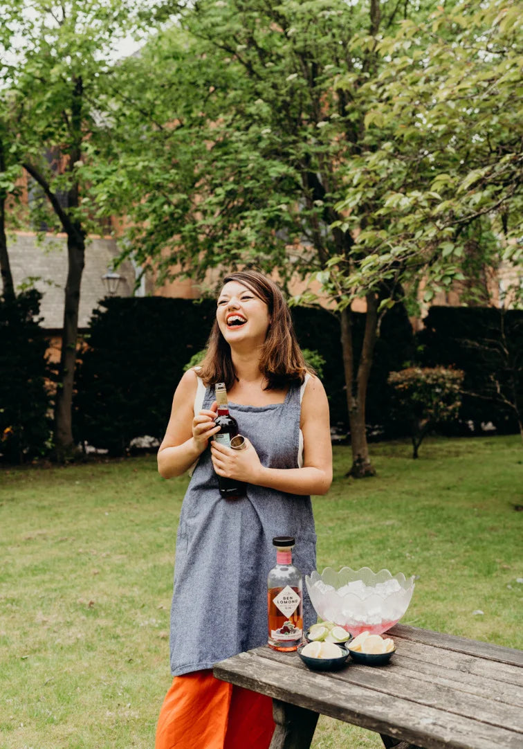 Woman laughing outdoors with a bottle of alcohol and snacks on a table