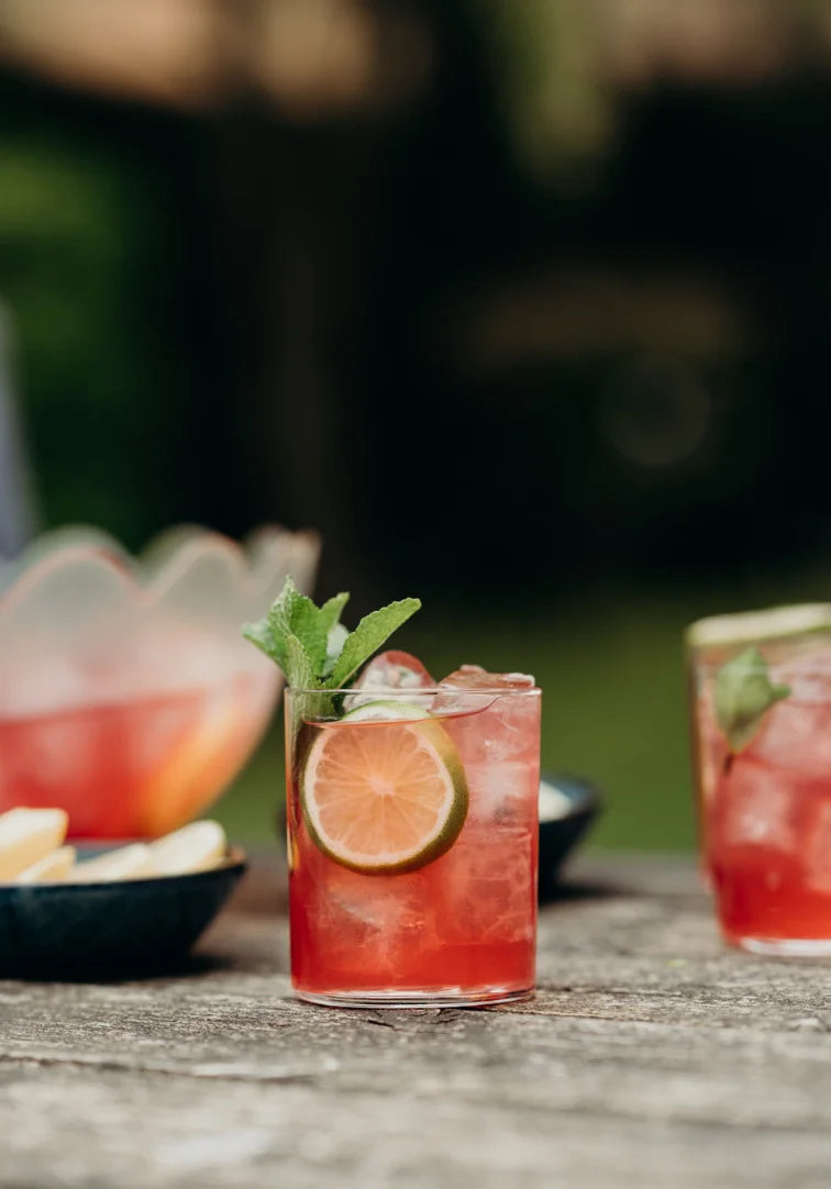 Cocktails with lime and mint garnishes on a wooden table outdoors.
