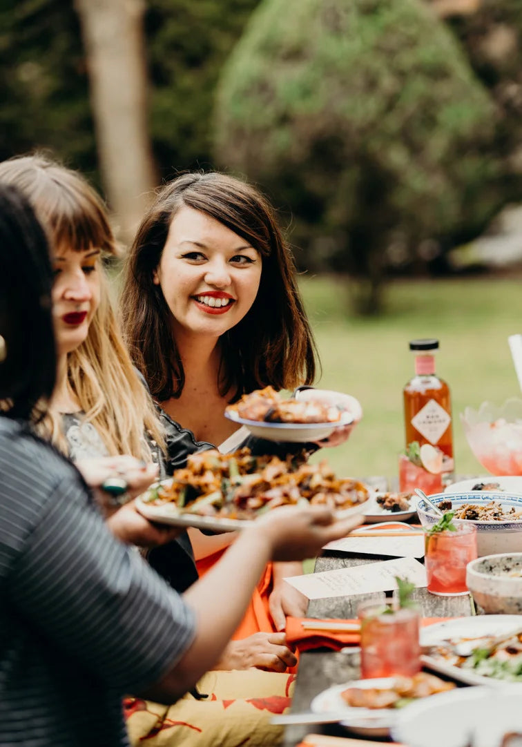 Three women enjoying a meal outdoors at a table with food and drinks.