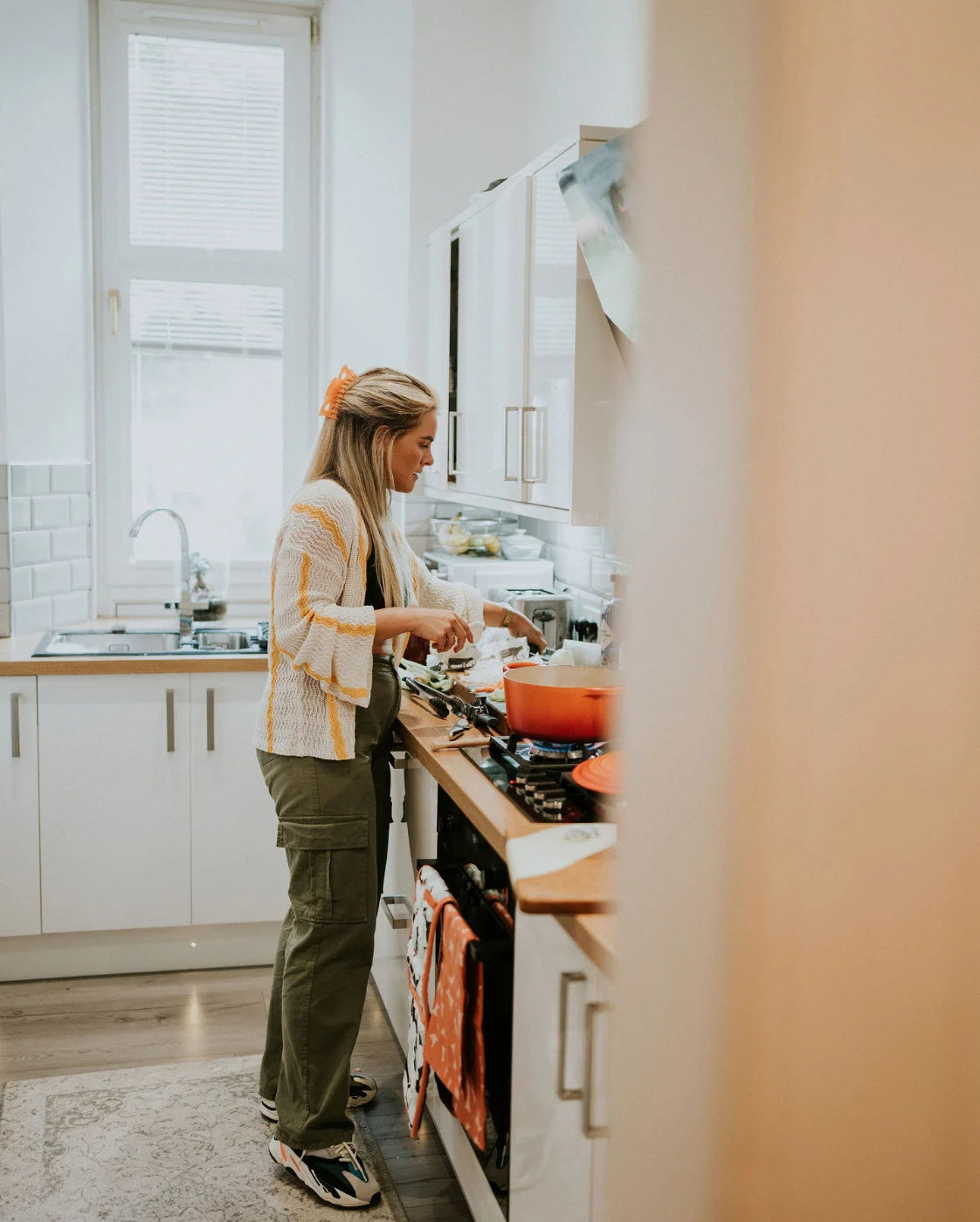 Person cooking in a modern kitchen with white cabinets and a window above the sink.