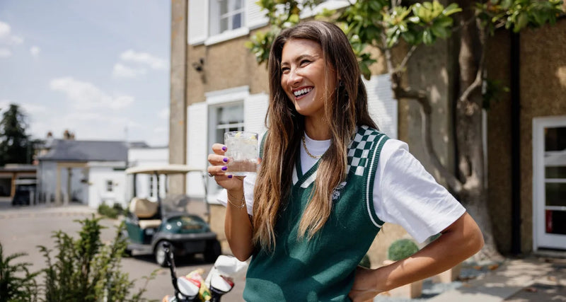 Woman in a green and white sports jersey holding a drink outdoors.