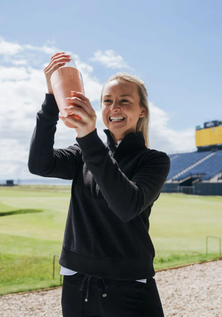 Woman in black outfit holding a cocktail shaker on a golf course