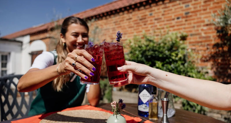 Two people clinking glasses of red cocktails outdoors with a brick building in the background.