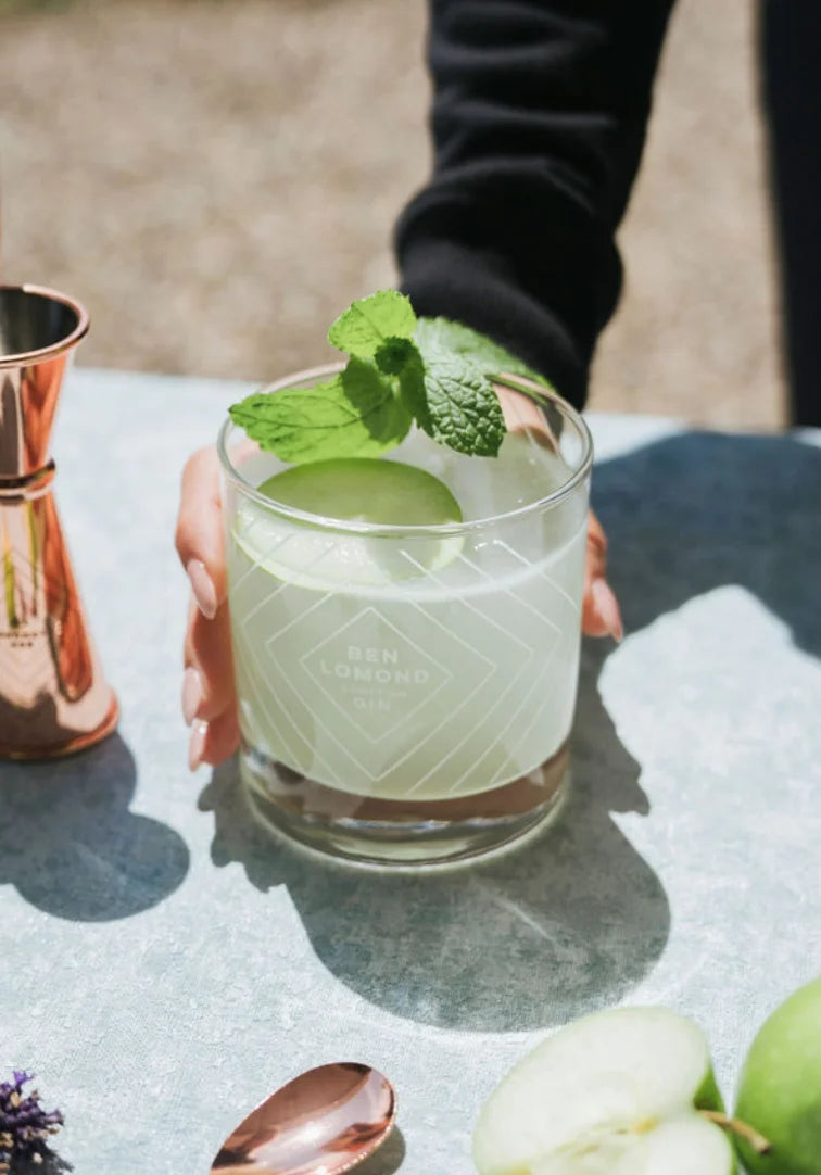 Green cocktail with a mint leaf in a glass, held by a person outdoors.