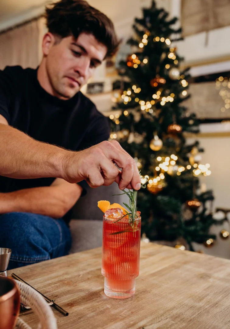 Man preparing a cocktail in front of a decorated Christmas tree