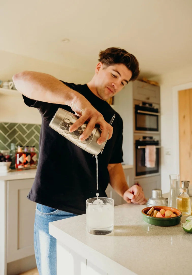 Person pouring a drink into a glass in a kitchen.