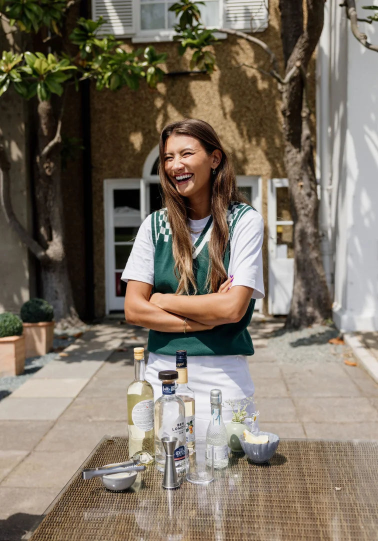 Woman standing outdoors with a table of drinks and bottles