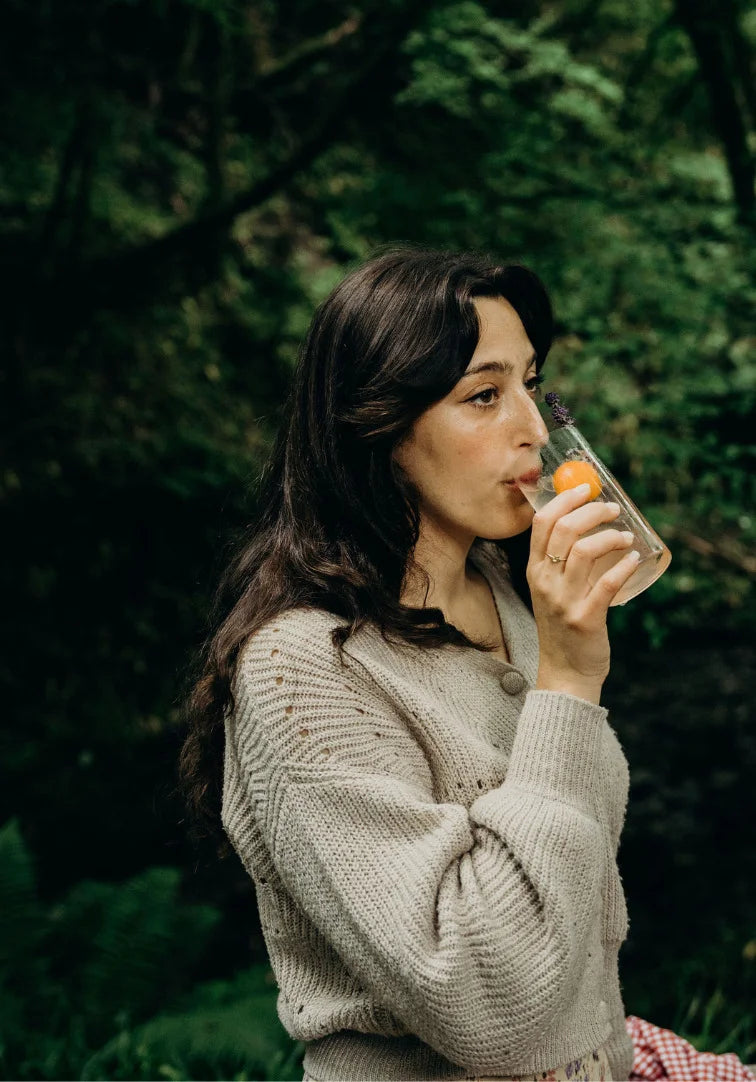 Woman drinking from a glass with fruit in a forest setting