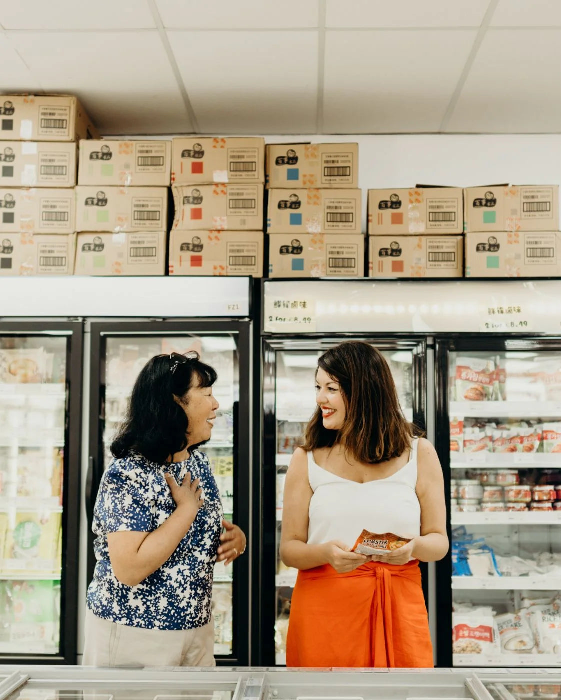 Two women standing in a freezer aisle of a grocery store.