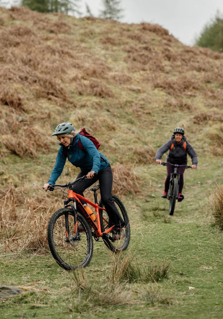 Two people riding bicycles on a grassy hillside.