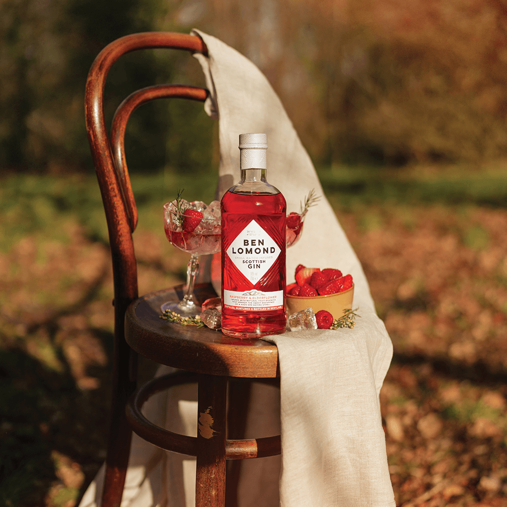 Ben Lomond gin bottle with a cocktail and strawberries on a wooden stool outdoors.