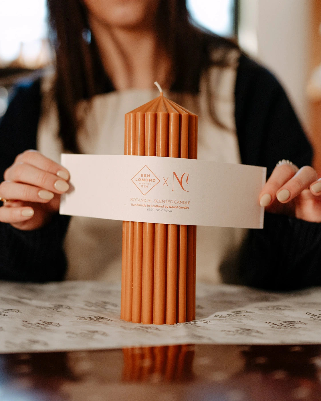Person holding a textured candle with a brand label against a blurred background
