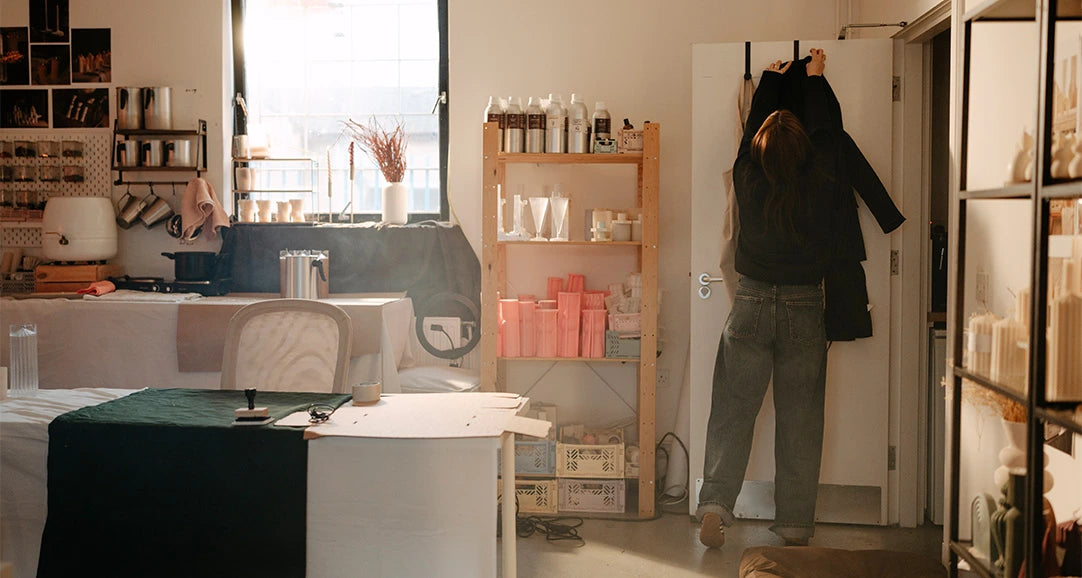 Person hanging a coat in a kitchen with shelves and a window in the background