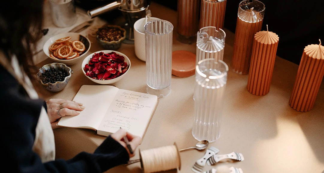 Person writing in a notebook with candles and decorative items on a table