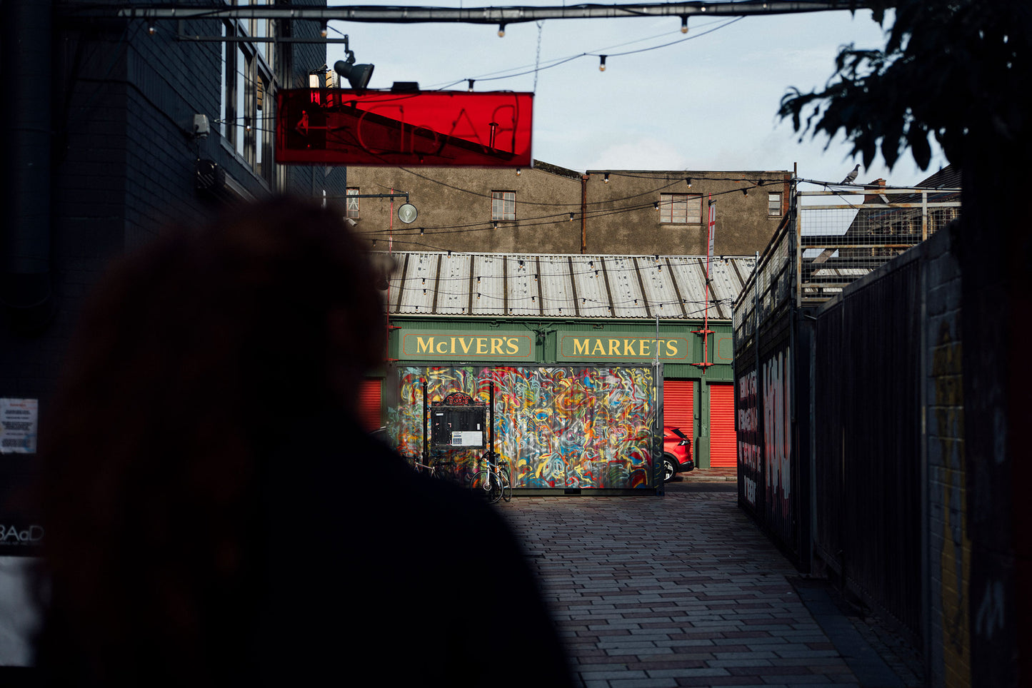 Silhouette of a person walking towards a market with a colorful mural on the wall.