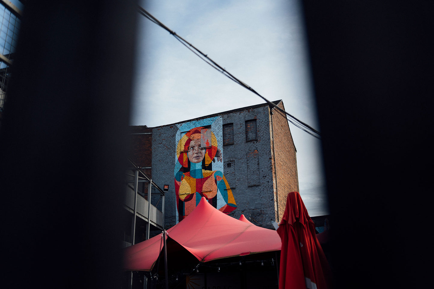 Colorful mural of a woman on a building with a red canopy in the foreground.