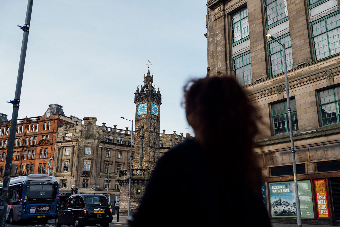 Person walking in a city street with a clock tower and buildings in the background