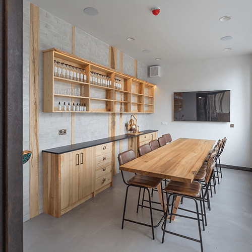 Modern botanical blending lab with wooden dining table and shelves, featuring a TV on the wall.