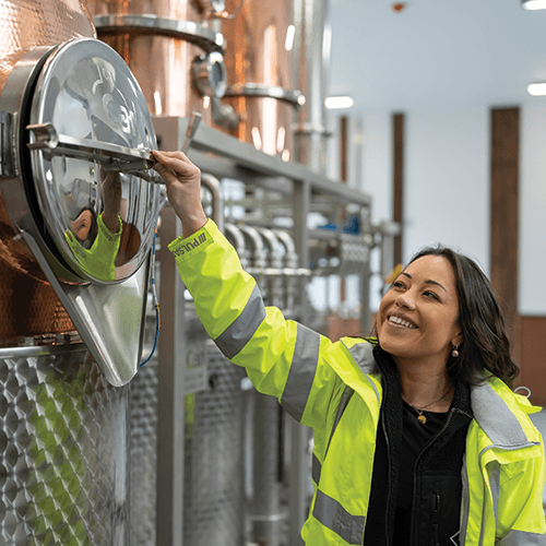 Person in a bright yellow safety jacket interacting with industrial equipment in a Gin Distillery setting.