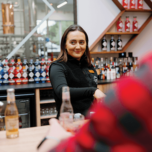 Person standing behind a bar with various Ben Lomond Gin bottles in the background.
