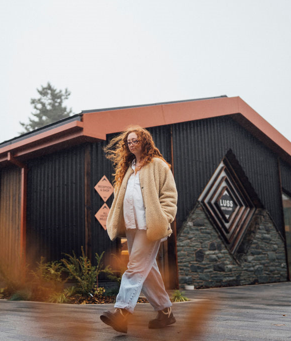 Woman walking outside a building with a 'Luss' sign in the background