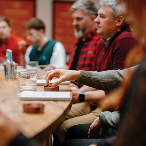 Group of people sitting around a table in a casual setting, with one person reaching out to pick something up.