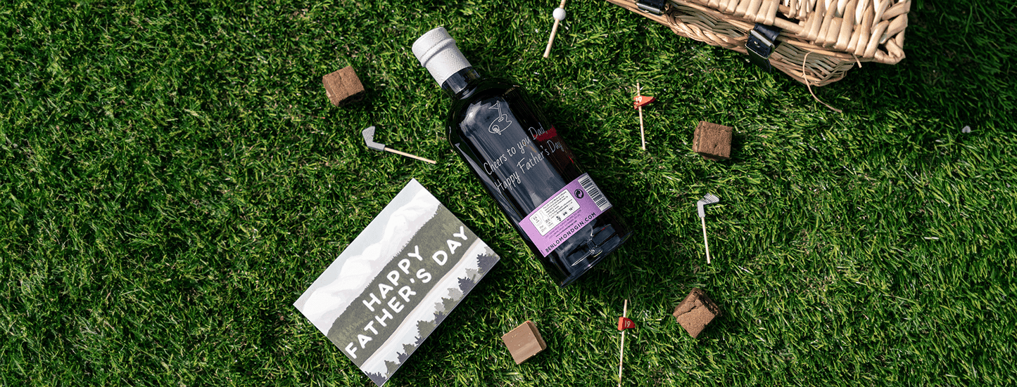 Bottle of wine, 'Happy Father's Day' card, and small items on grass