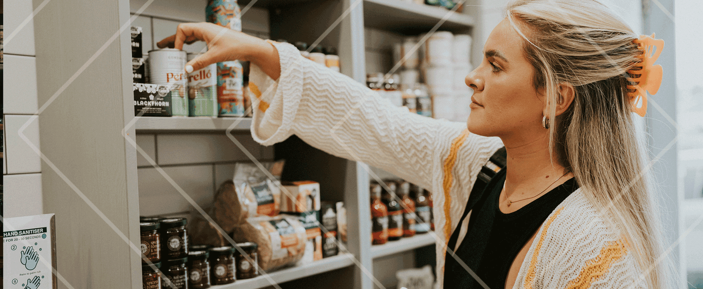 Woman shopping in a store aisle, reaching for a product on a shelf.