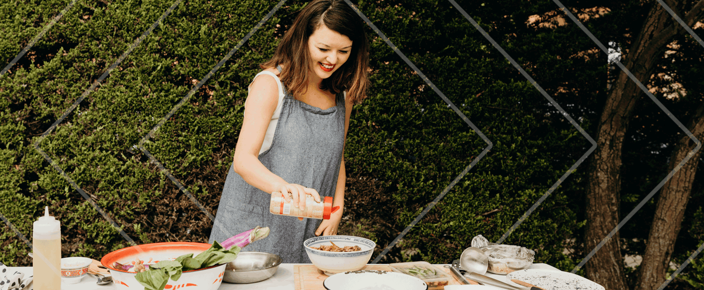 Woman preparing food outdoors at a table with a garden background