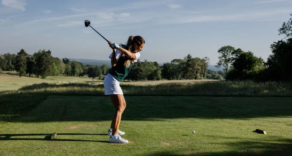 Woman playing golf on a green course with trees in the background