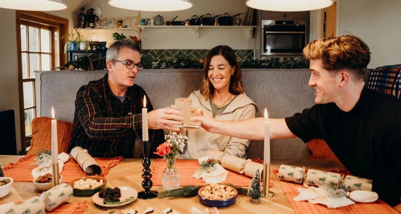 Three people sitting around a dinner table with candles and food, smiling and toasting.