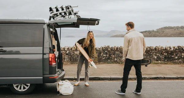 Two people with surfboards near a van by a lake.