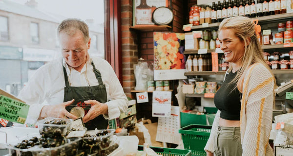Man and woman in a store, man behind a counter with produce, woman standing next to him