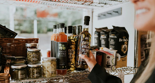 Assorted food items including bottles, jars, and a person holding a bottle of olive oil on a shelf.