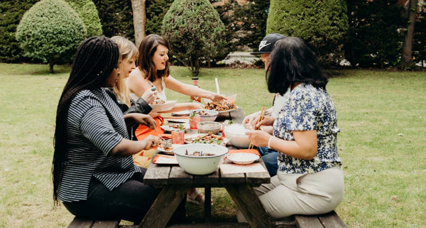 Group of people sitting around a wooden picnic table outdoors, enjoying a meal.