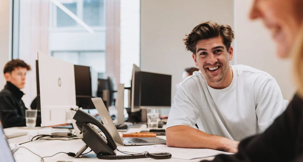 Person sitting at a desk in an office with another person partially visible