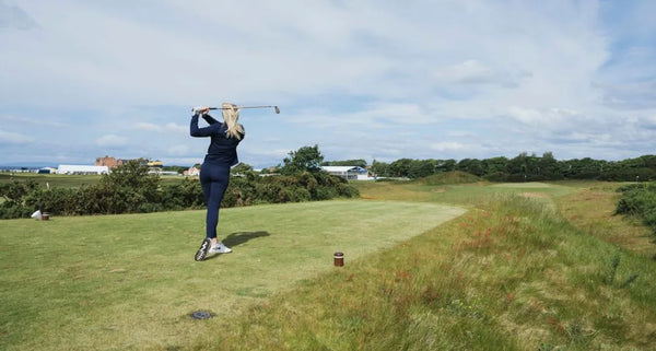 Person playing golf on a grassy field with trees and buildings in the background