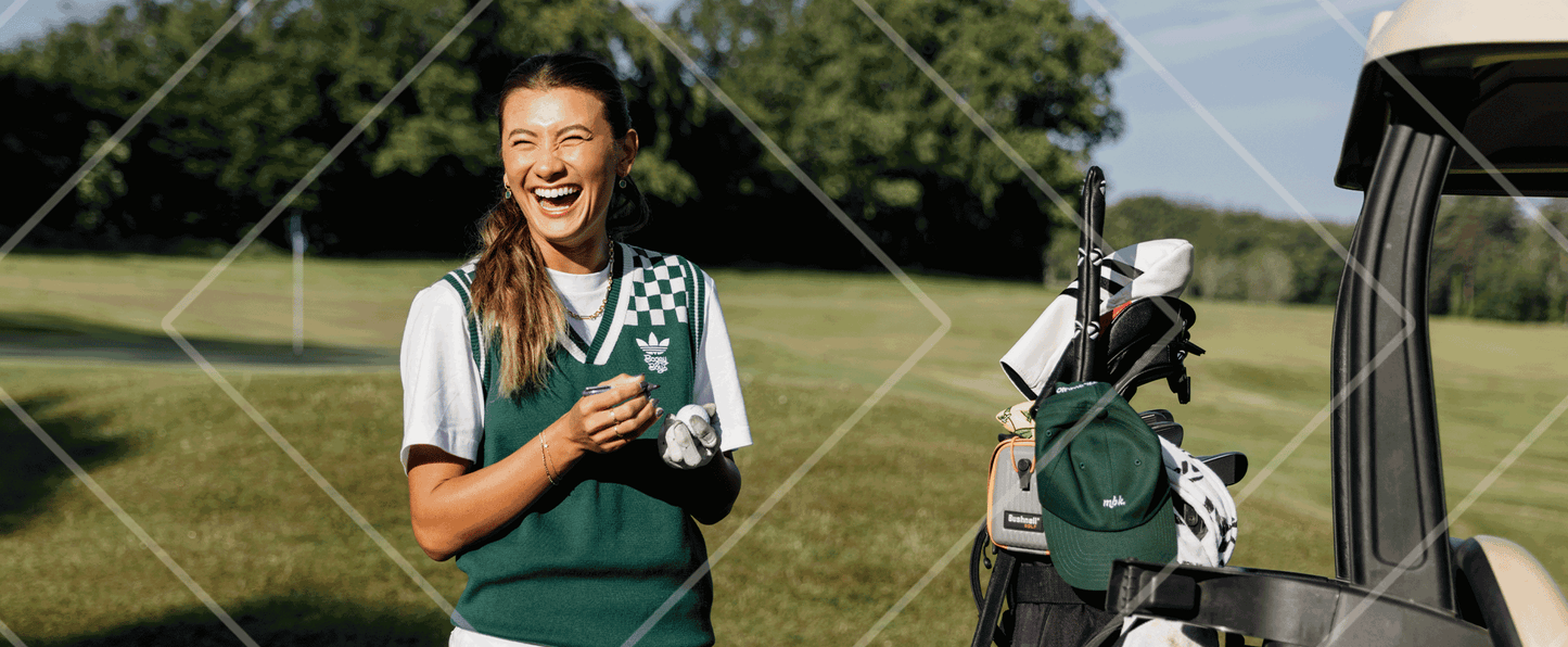 Woman in a green and white golf outfit standing next to a golf cart with clubs on a golf course.